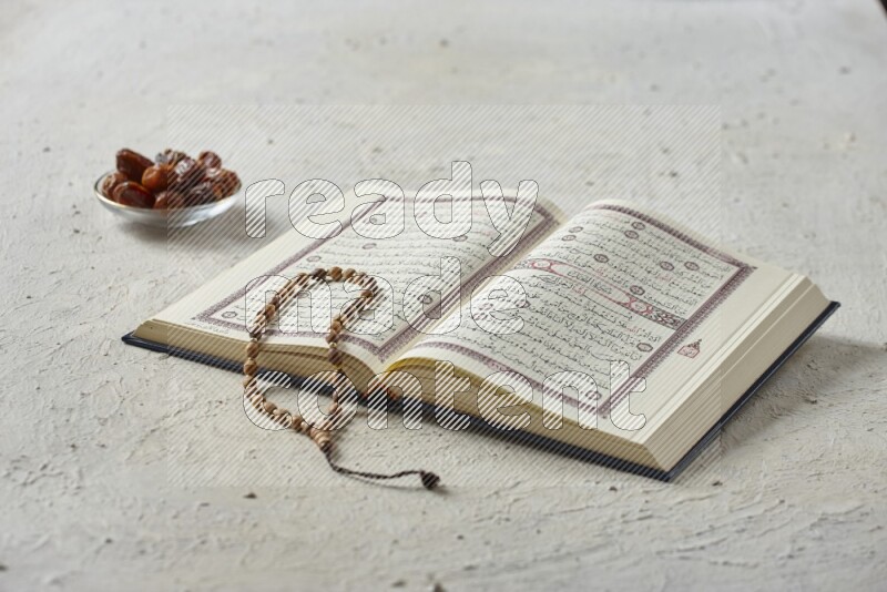 Quran with dates, prayer beads and different drinks all placed on textured white background
