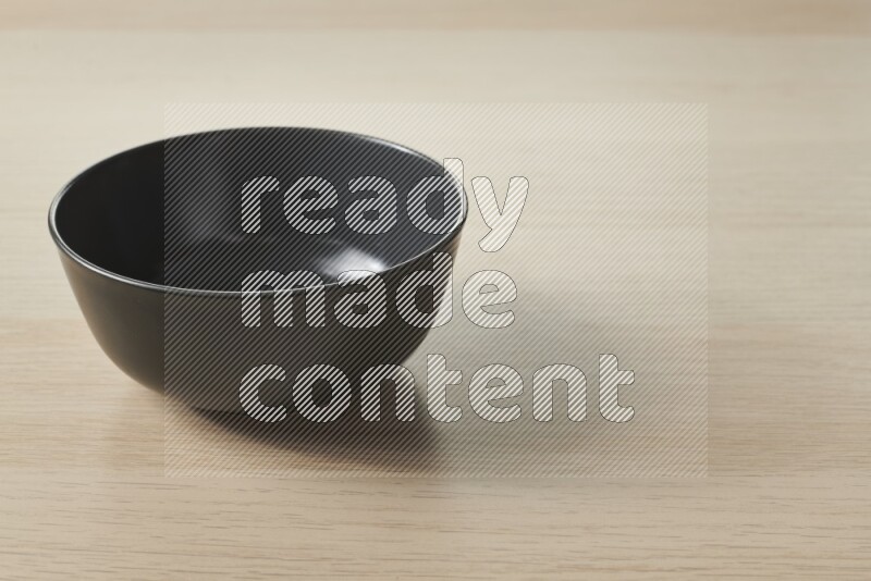 A black ceramic bowl on light wooden background