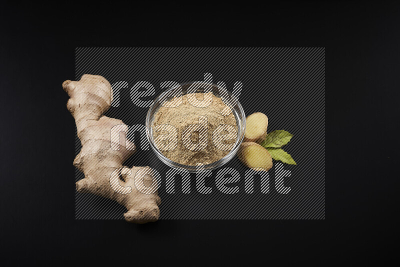 A glass bowl full of ground ginger powder on black background