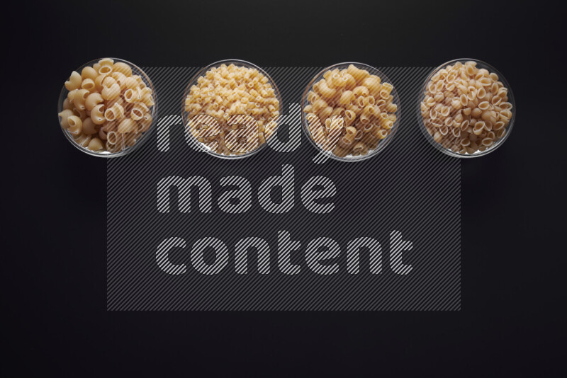 Different pasta types in glass bowls on black background