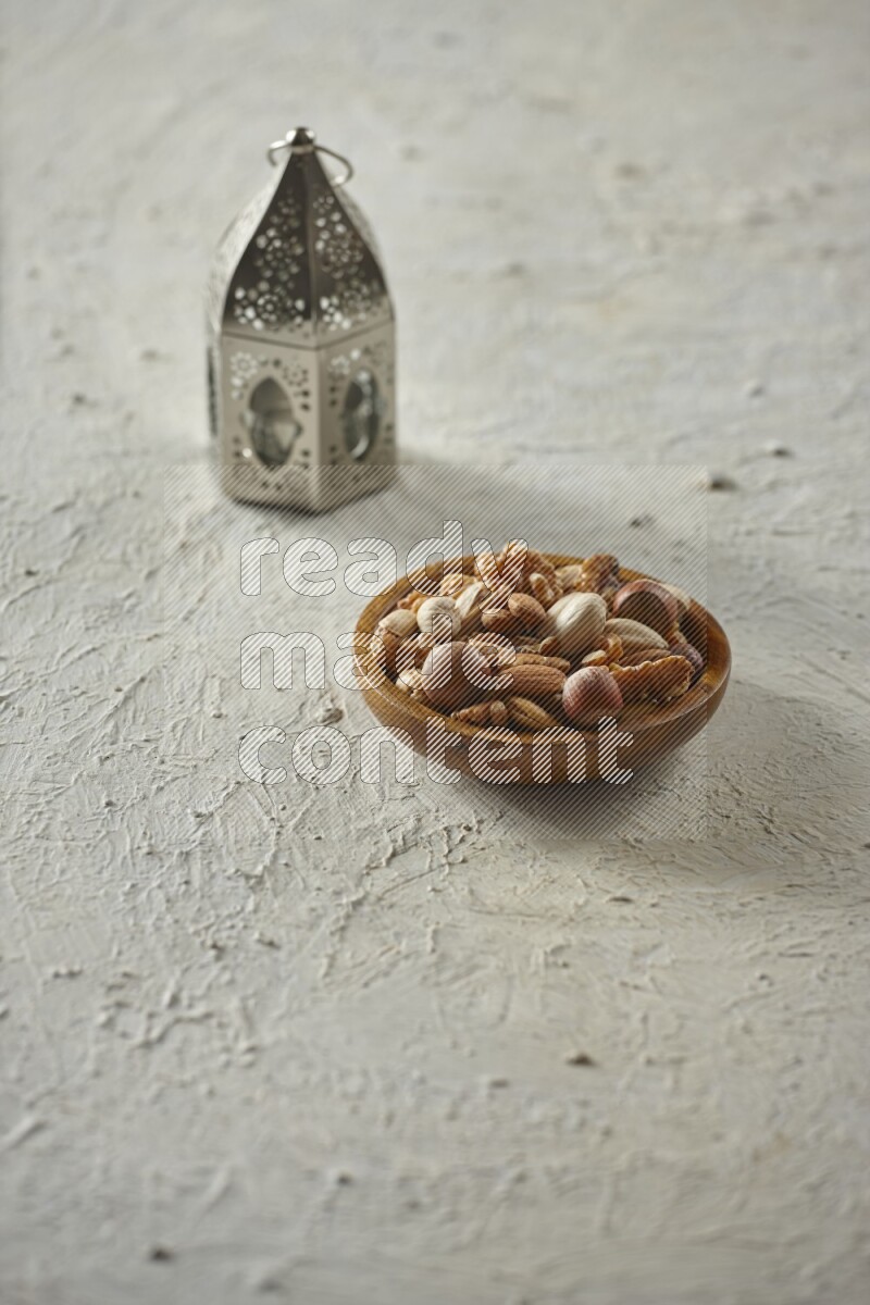 A silver lantern with different drinks, dates, nuts, prayer beads and quran on textured white background