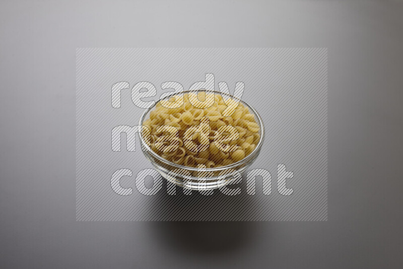 Shells pasta in a glass bowl on grey background