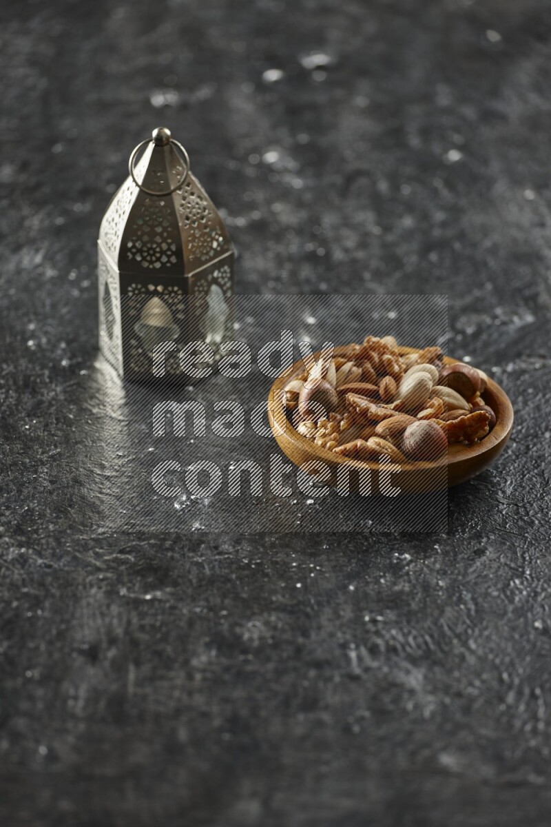 A silver lantern with different drinks, dates, nuts, prayer beads and quran on textured black background