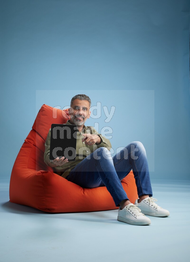 A man sitting on an orange beanbag and working on tablet