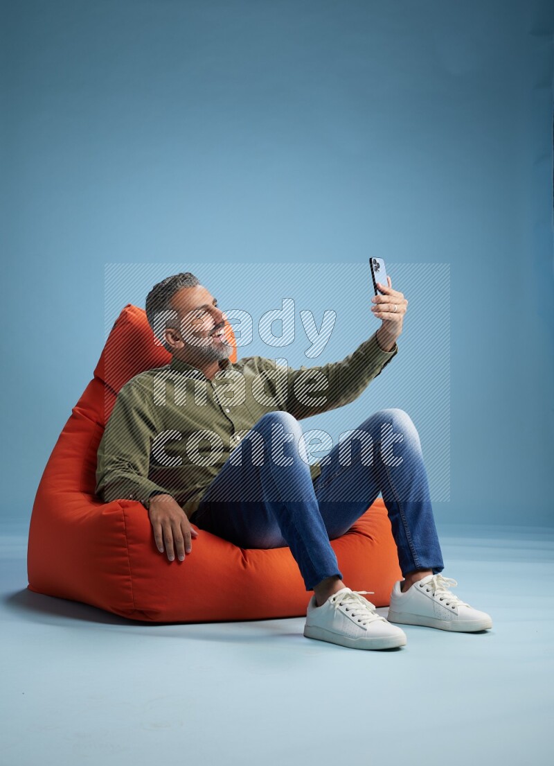 A man sitting on an orange beanbag and taking selfie