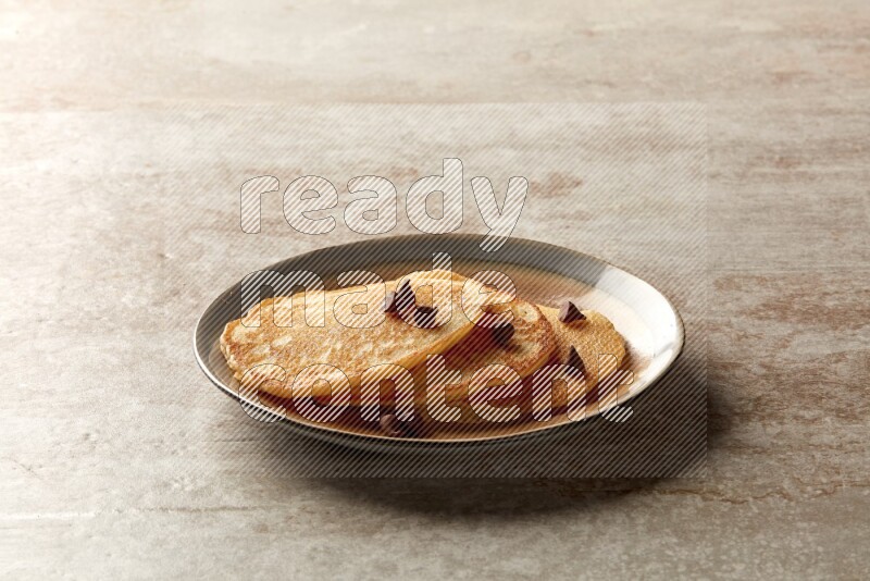Three stacked chocolate chips pancakes in a bicolor plate on beige background