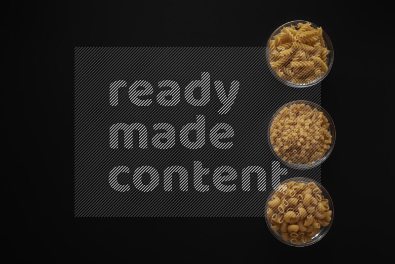 Different pasta types in 3 glass bowls on black background