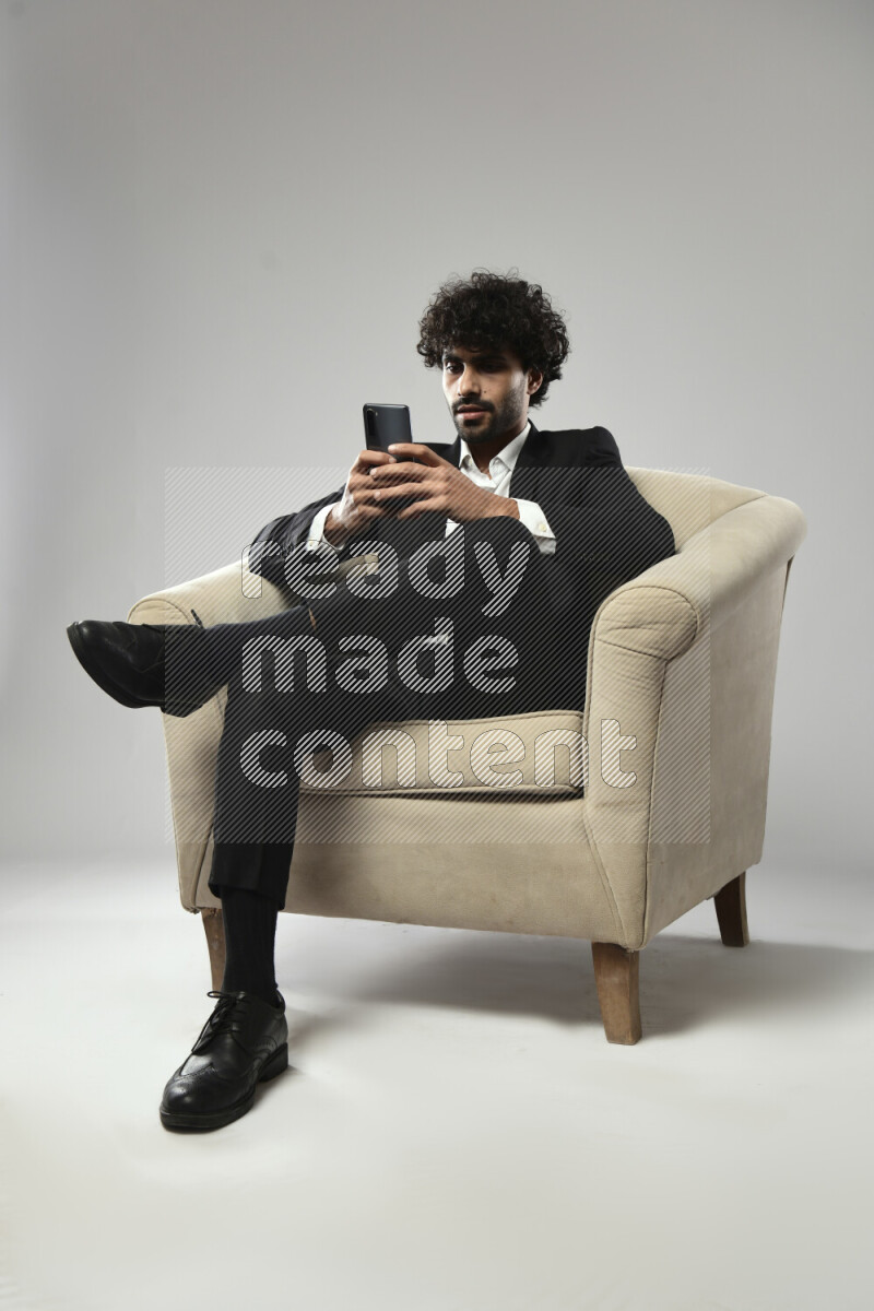 A man wearing formal sitting on a chair texting on the phone on white background