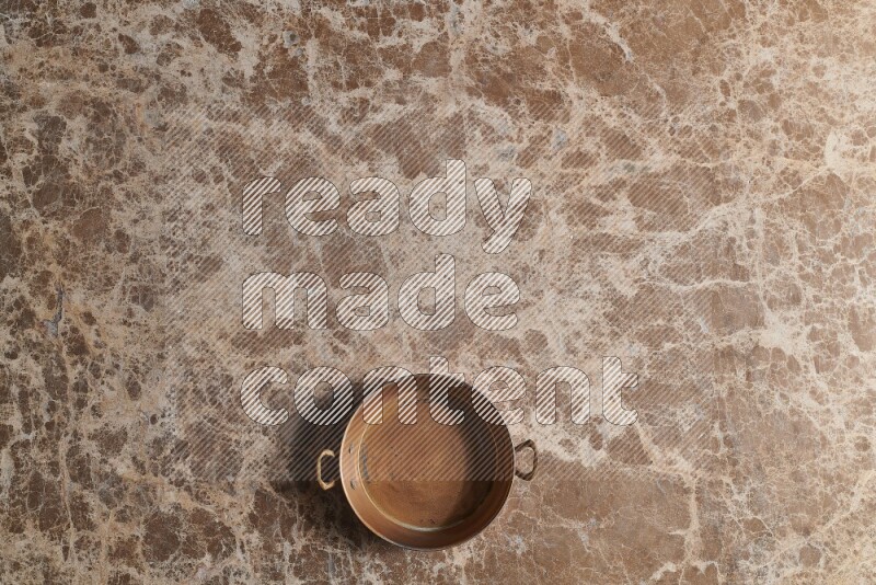 A small copper pan on beige marble background