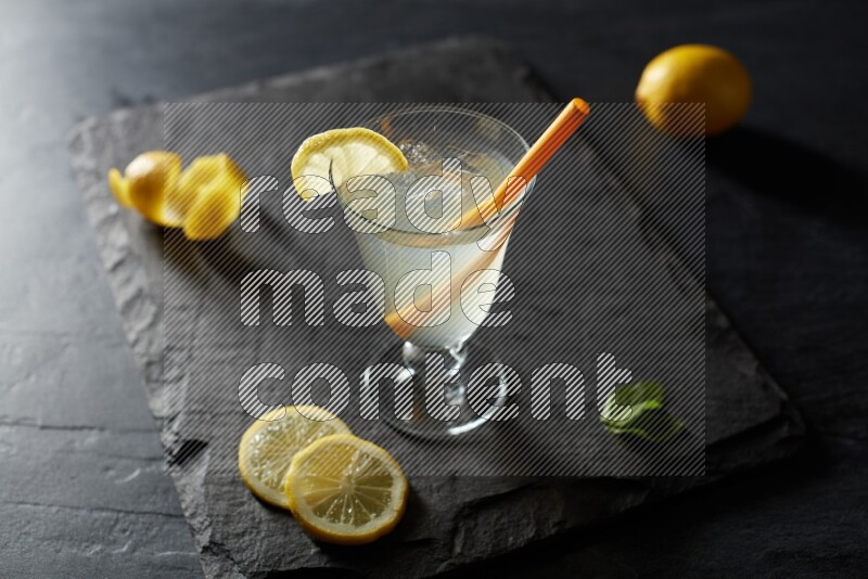 A glass of lemon juice with a straw on black background