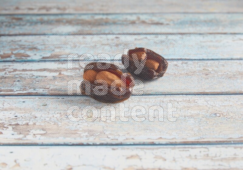 two almond stuffed madjoul dates on a light blue wooden background