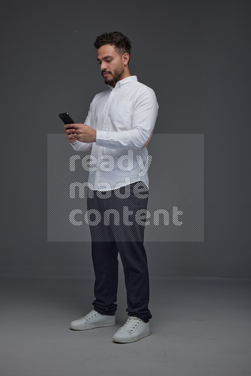 A man wearing smart casual standing and using his phone eye level on a gray background