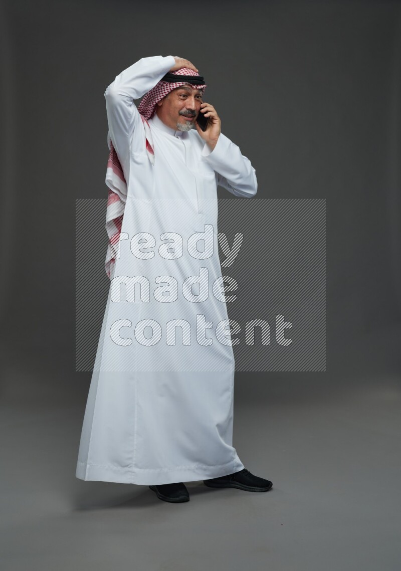 Saudi man with shomag Standing talking on phone on gray background