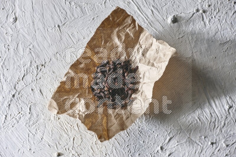 Cloves on crumpled piece of paper on a textured white flooring