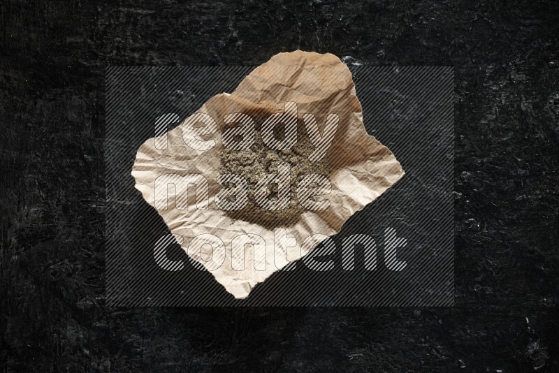 Cardamom powder in a crumpled piece of paper on textured black flooring