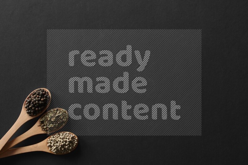 wooden spoons filled with white peppers, cloves, cardamom, salt, black peppers and basil on black flooring