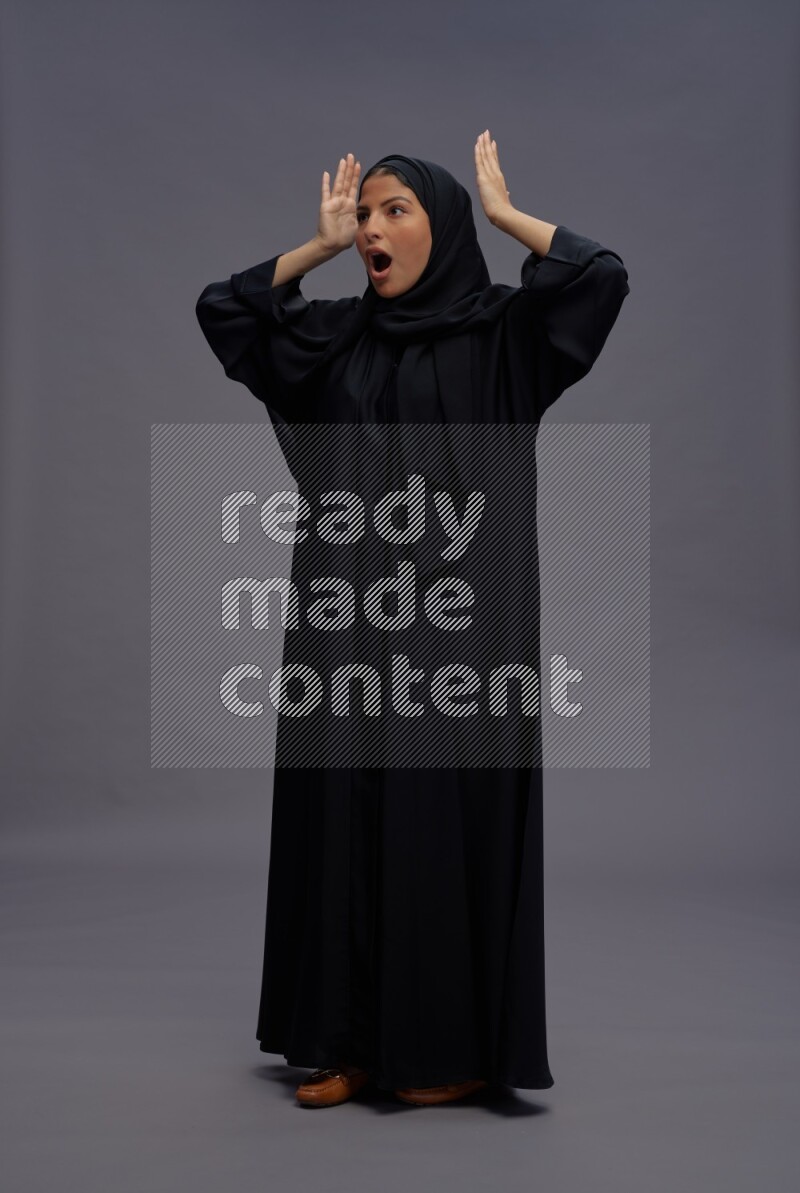 Saudi woman wearing Abaya standing hands behind head on gray background