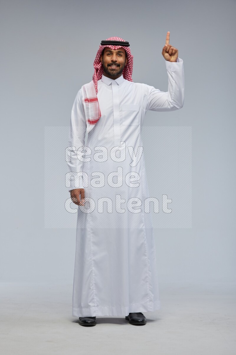Saudi man Wearing Thob and shomag standing interacting with the camera on Gray background