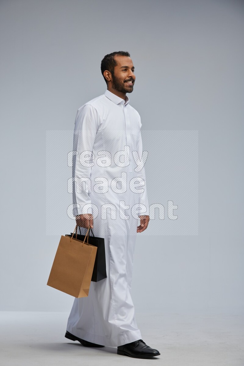 Saudi man Wearing thob standing holding shopping bag on Gray background