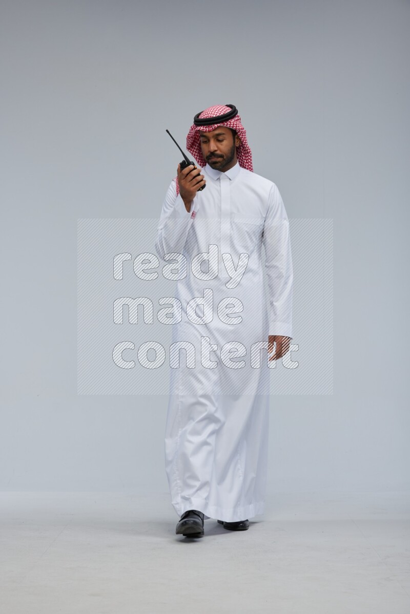 Saudi man Wearing Thob and shomag standing holding walkie-talkie on Gray background