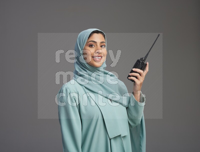 Saudi Woman wearing Abaya standing holding walkie-talkie on Gray background