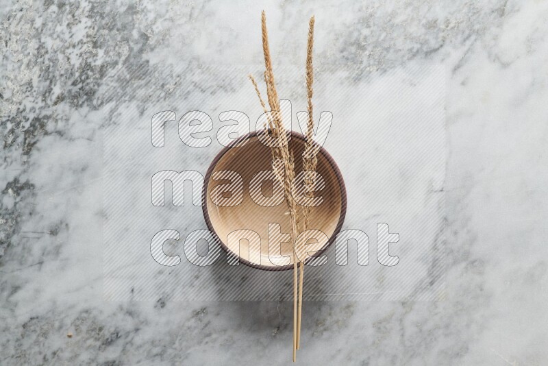 Wheat stalks on beige pottery oven bowl on grey marble background