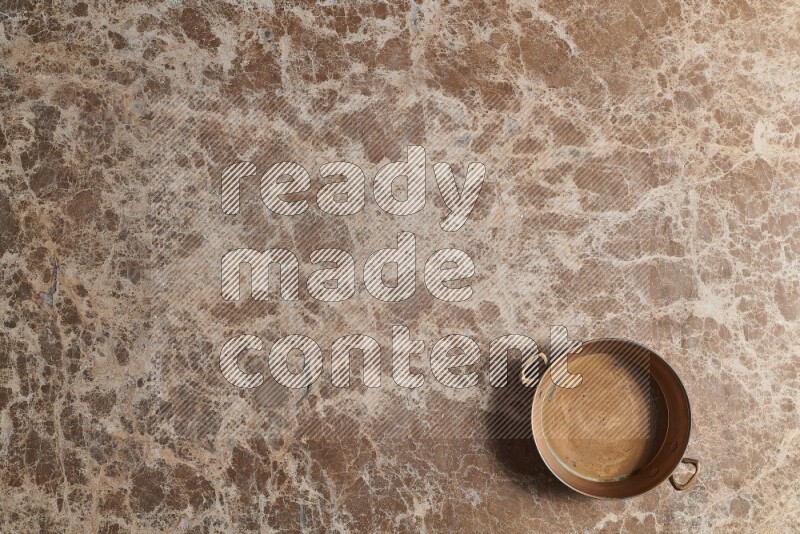 A small copper pan on beige marble background