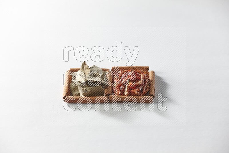 مربعان من أعواد القرفة ممتلئان بالفلفل الحار المجفف وأوراق الغار علي خلفية بيضاء