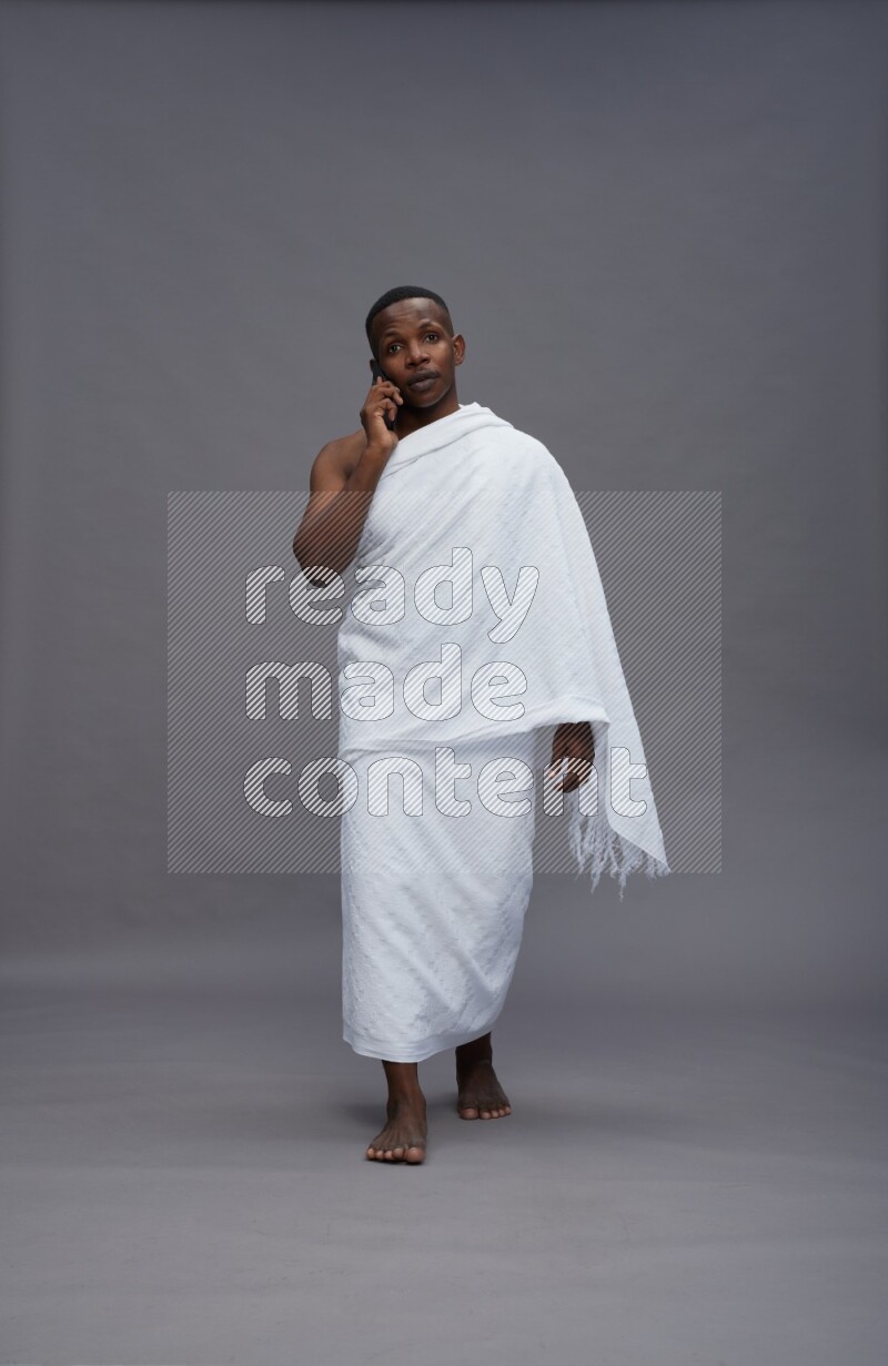 A man wearing Ehram Standing talking on phone on gray background