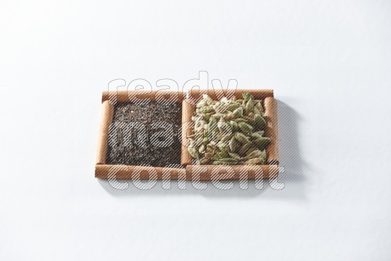 مربعان من أعواد القرفة ممتلئان بالشاي الأسود وحبوب الهال علي خلفية بيضاء