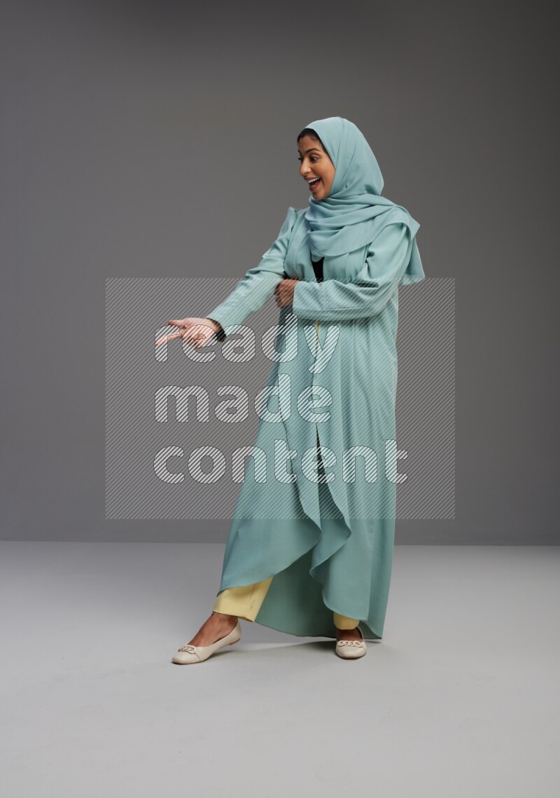 Saudi Woman wearing Abaya standing interacting with the camera on Gray background