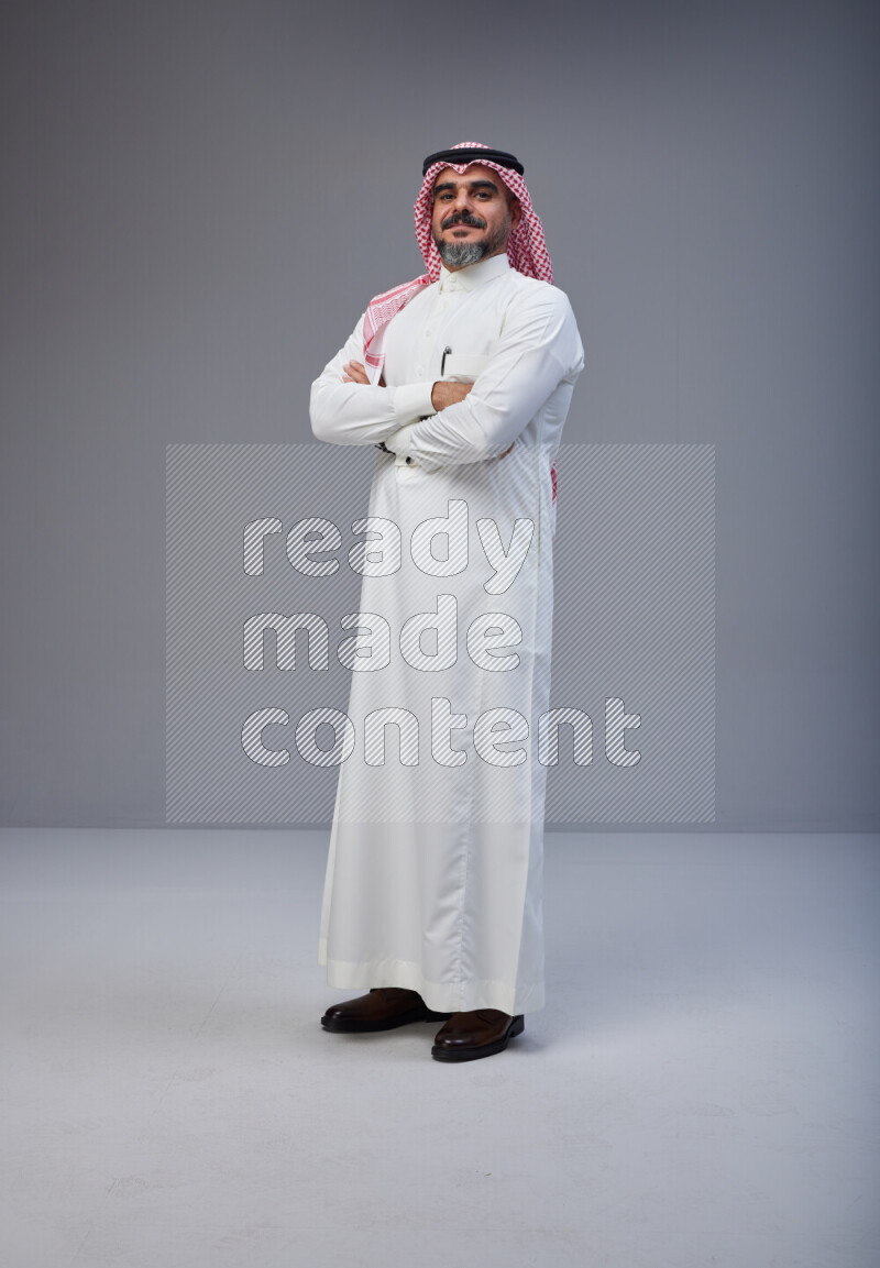 Saudi man Wearing Thob and red Shomag standing with crossed arms on Gray background