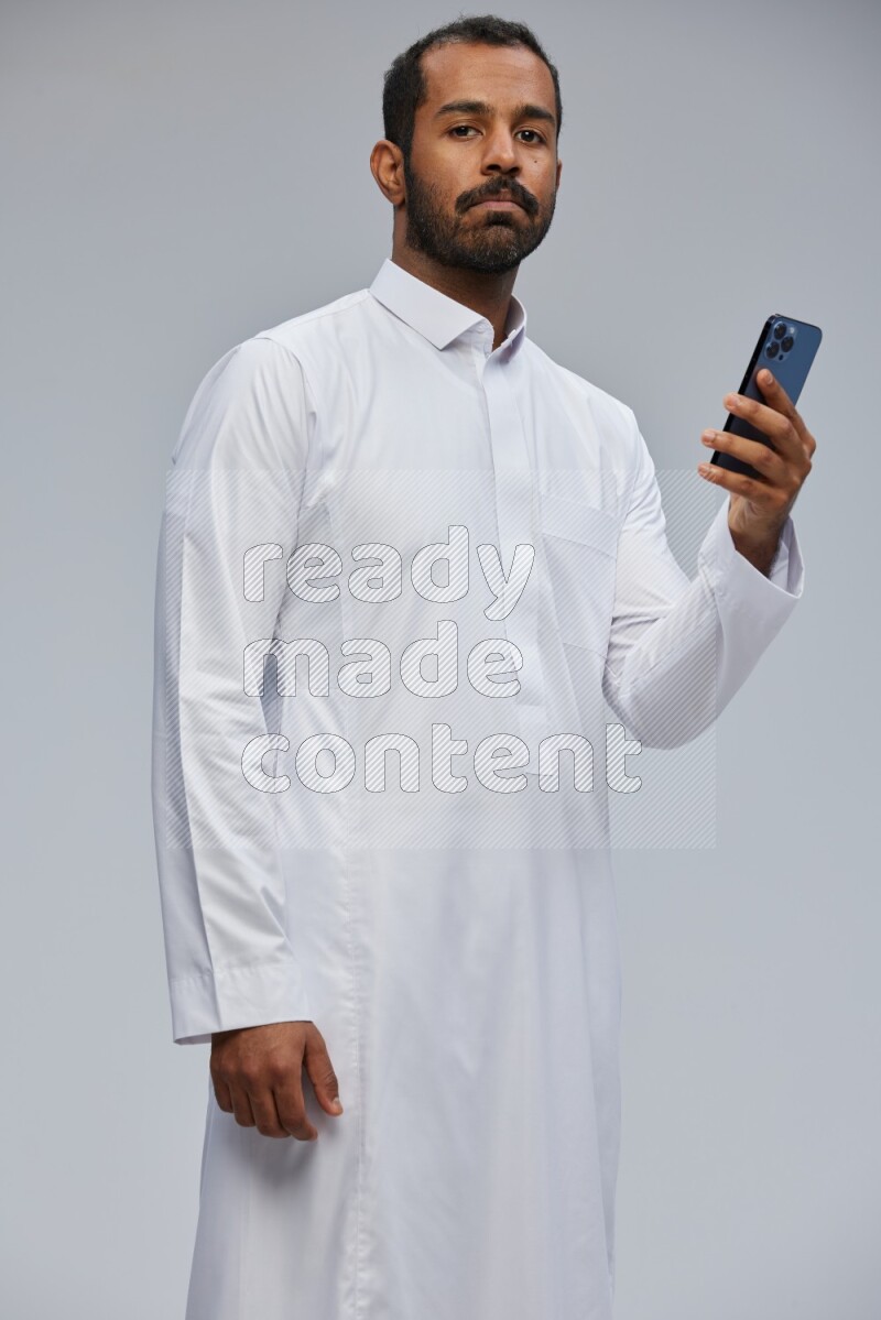 Saudi man wearing Thob standing texting on phone on Gray background