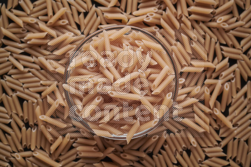 Mini penne pasta in a glass bowl on black background
