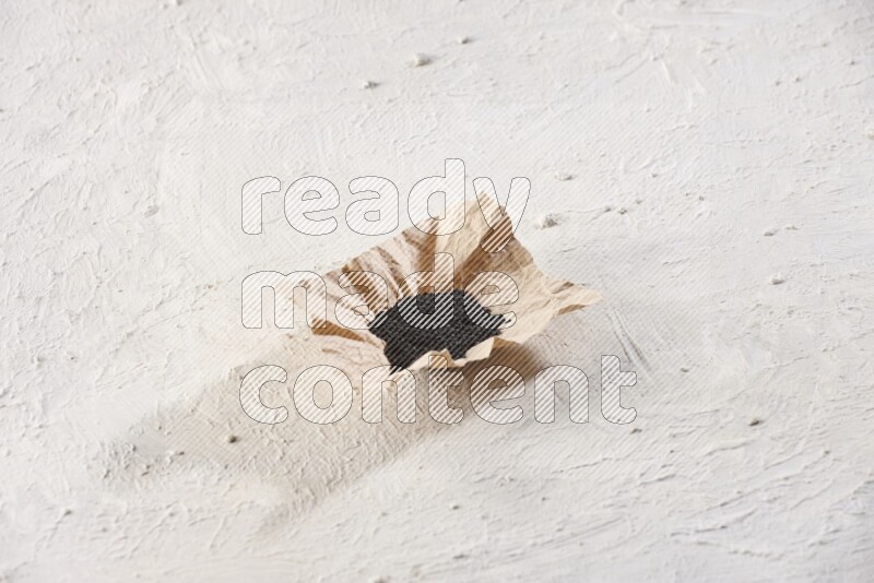 A crumpled piece of paper full of black seeds on a textured white flooring