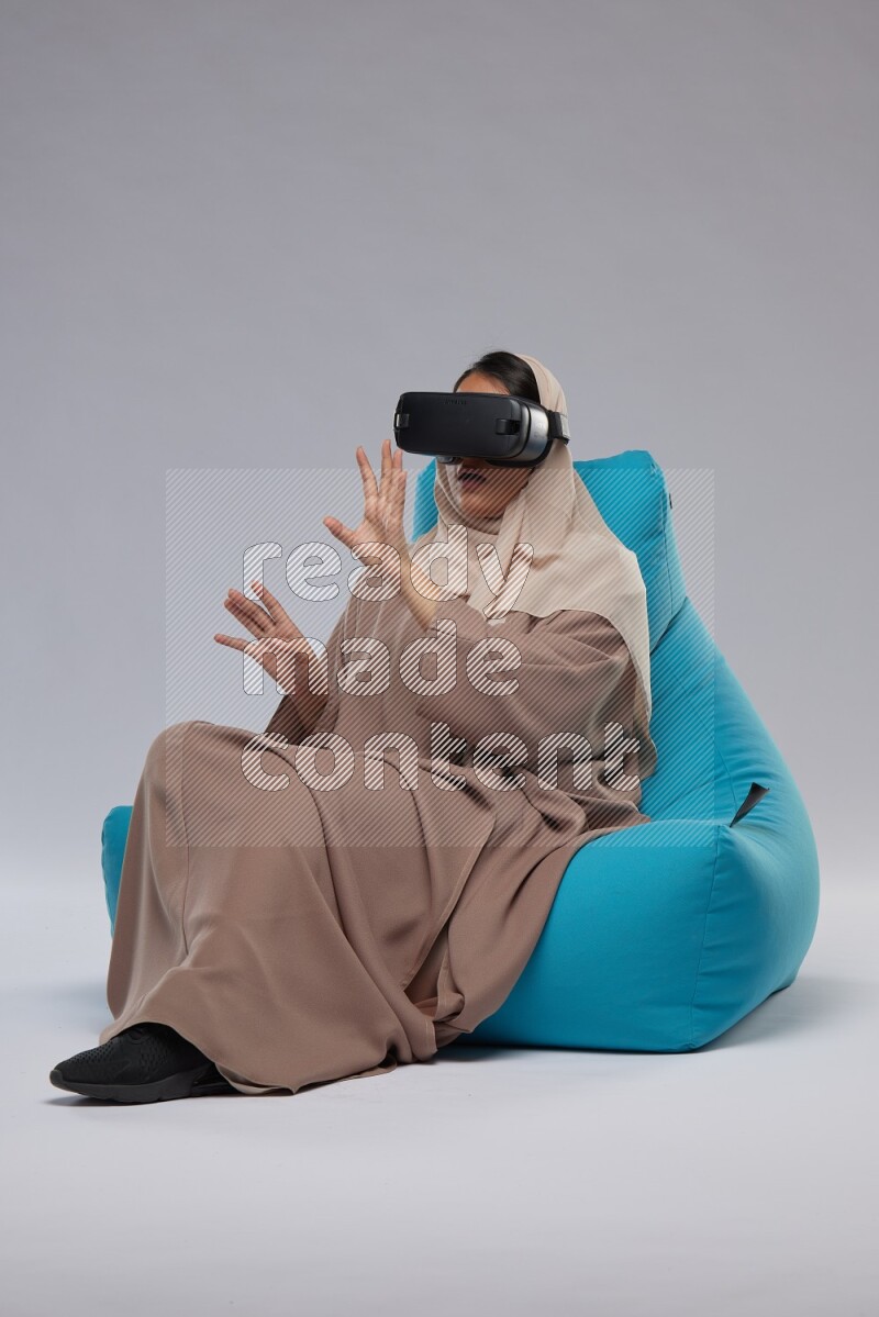 A Saudi woman sitting on a blue beanbag and gaming with VR