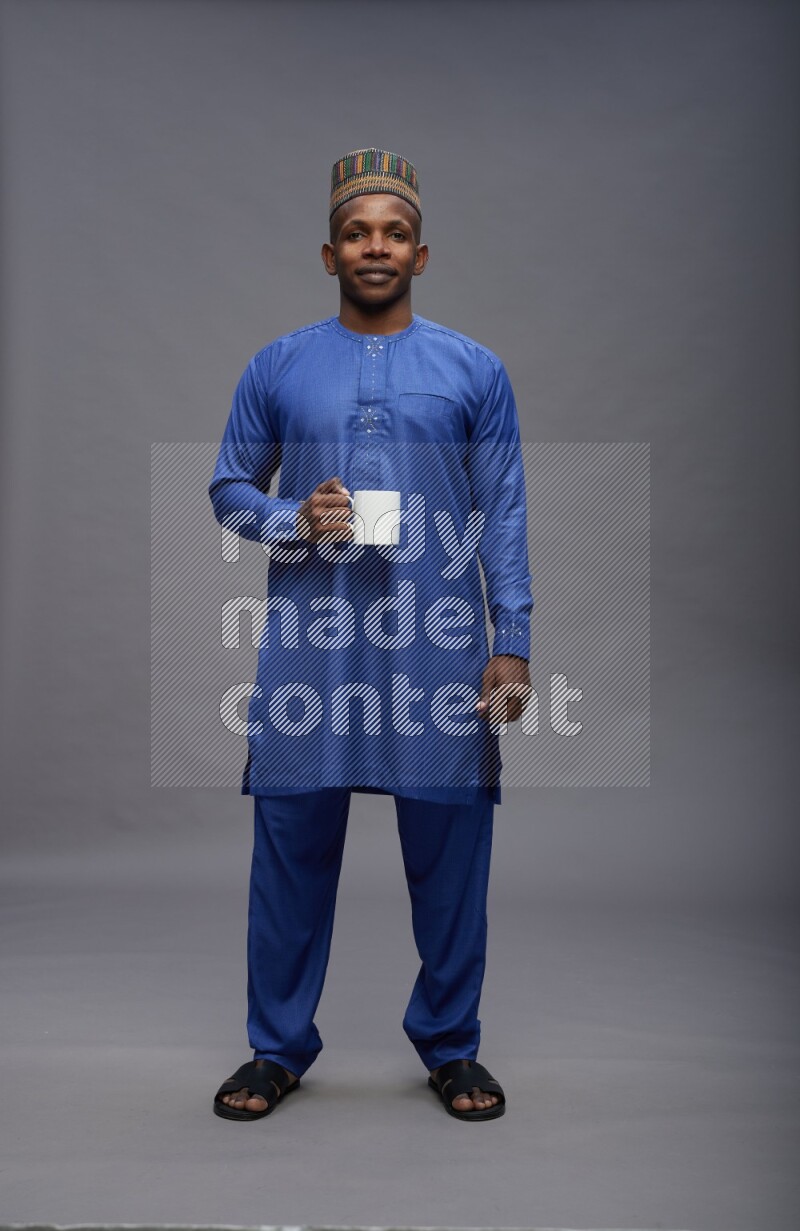 Man wearing Nigerian outfit standing holding mug on gray background