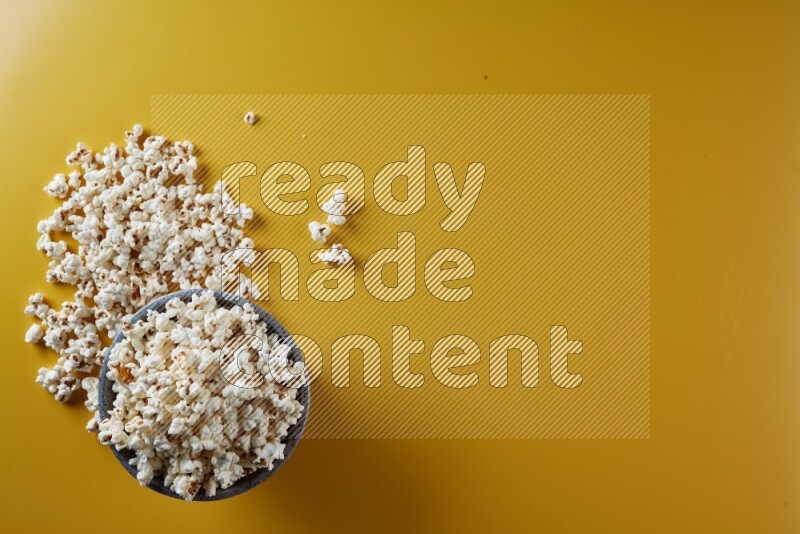 A multicolored pottery bowl full of popcorn with popcorn beside it on a yellow background in different angles
