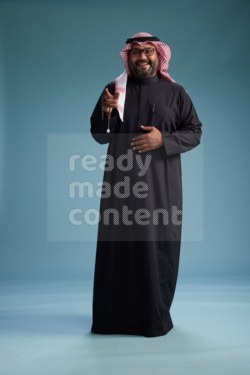 Saudi Man with shimag Standing Interacting with the camera on blue background