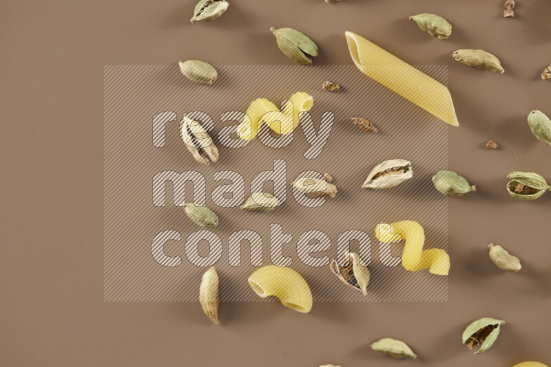 Raw pasta with different ingredients such as cherry tomatoes, garlic, onions, red chilis, black pepper, white pepper, bay laurel leaves, rosemary and cardamom on beige background