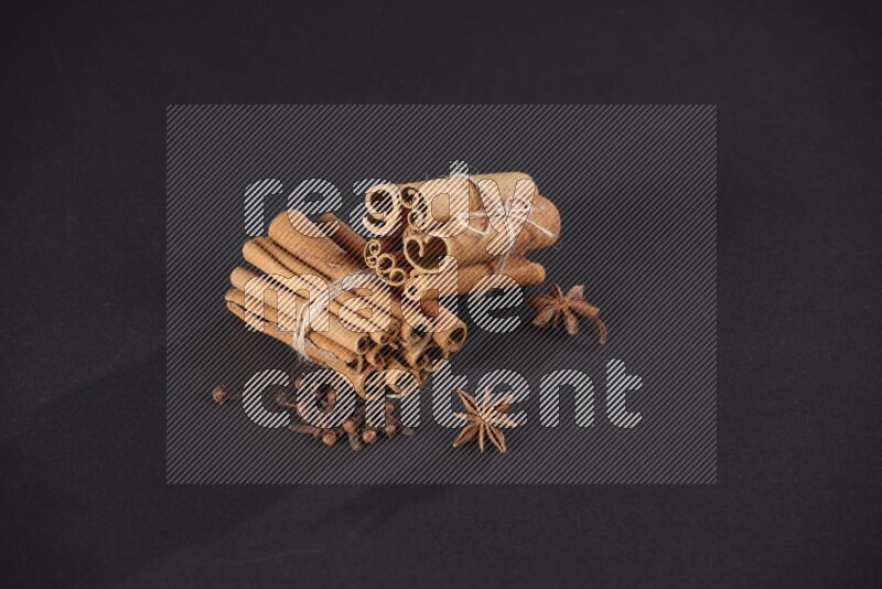 Two bounded stacks of cinnamon sticks with cloves and star anise on black background