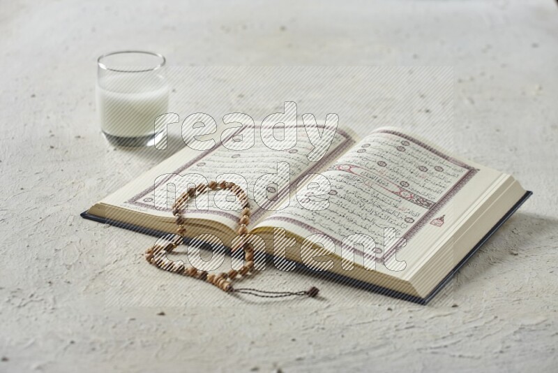 Quran with dates, prayer beads and different drinks all placed on textured white background