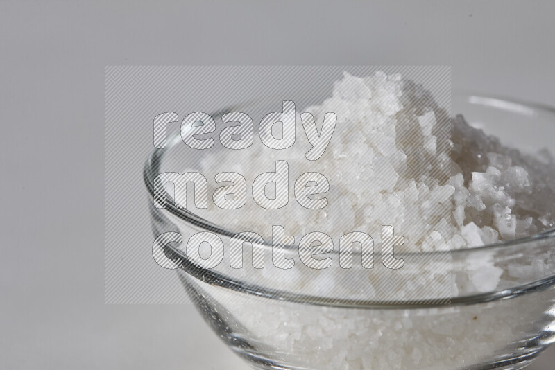 A glass bowl full of coarse sea salt crystals on white background