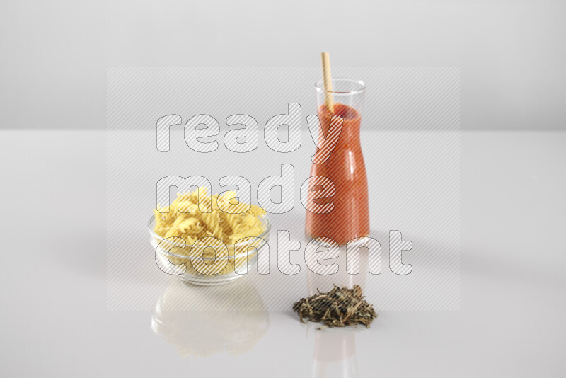 Raw pasta with tomatoe pasta with different ingredients such as cherry tomatoes, basil, garlic, bay laurel, cardamom, white pepper, black pepper, red chilis and wheat stalks on light grey background