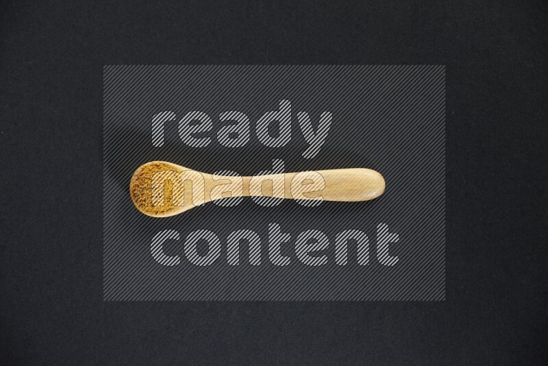 ملعقة خشبية ممتلئة ببودرة الكركم على خلفية سوداء