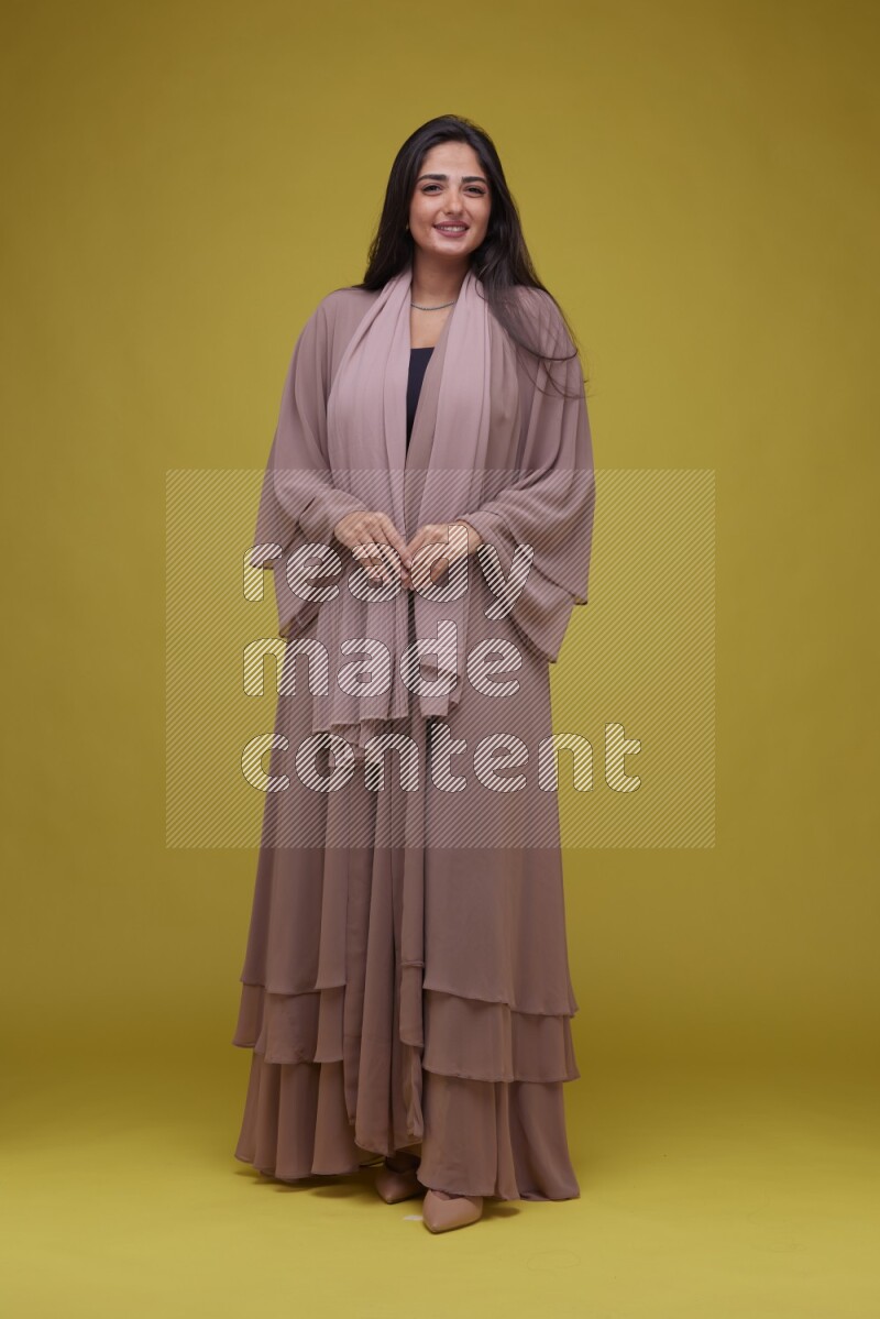 A woman Posing on a Yellow Background wearing Brown Abaya