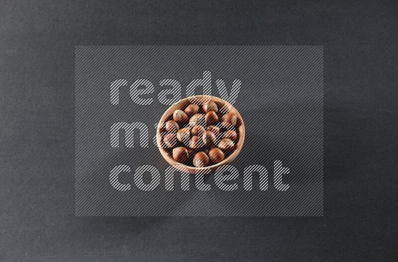 A wooden bowl full of hazelnuts on a black background in different angles