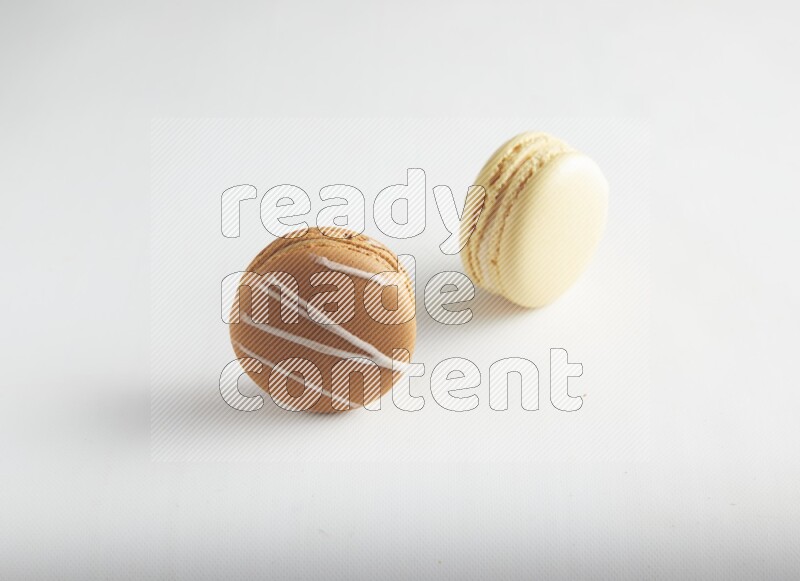 45º Shot of of two assorted Brown Irish Cream, and Yellow Vanilla macarons on white background