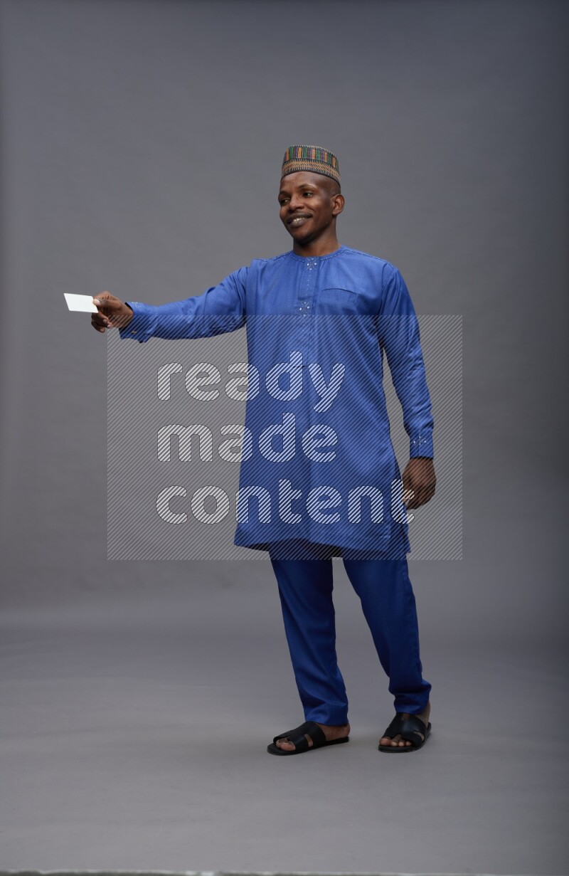 Man wearing Nigerian outfit standing holding ATM card on gray background