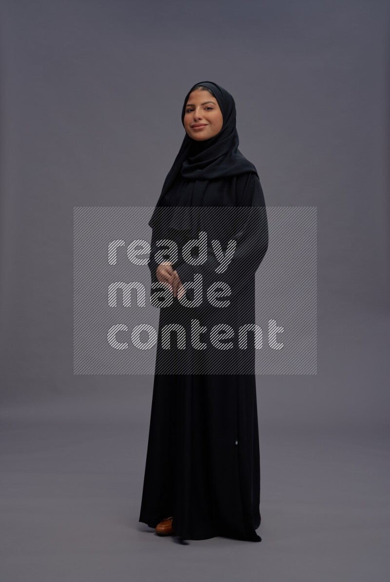 Saudi woman wearing Abaya standing interacting with the camera on gray background